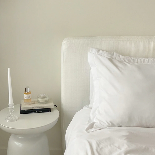 A clean fabric bed frame designed by SoftFrame Designs with white bedding and a nightstand with books and a candle on it