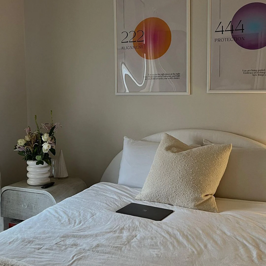 A Luna bed frame from SoftFrame Designs with white bedding, a laptop on the bed, and fresh flowers on the bedside table