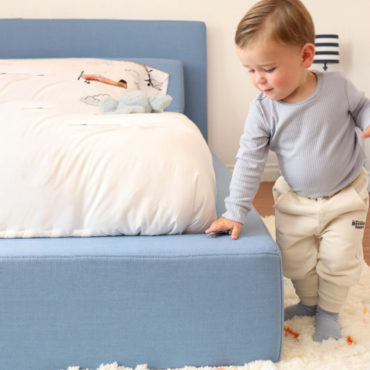 A toddler next to his upholstered bed frame from SoftFrame Designs