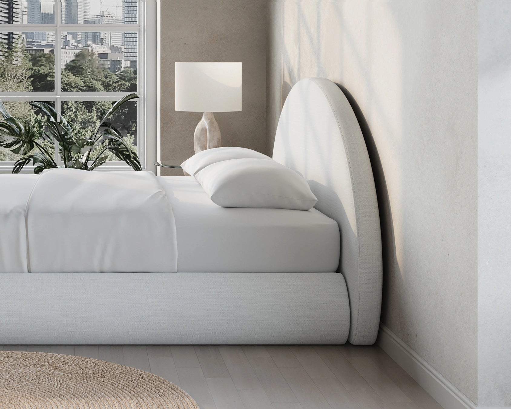 Modern bedroom with a curved all cushioned headboard, lamp, and window view of trees.