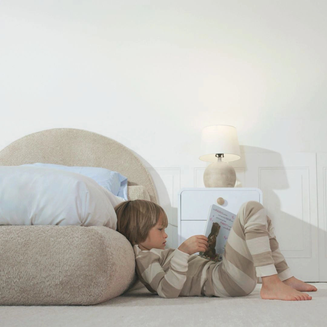 Boy reading a book on the side rail of a all cushioned rounded bed frame