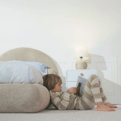Boy reading a book on the side rail of a all cushioned rounded bed frame