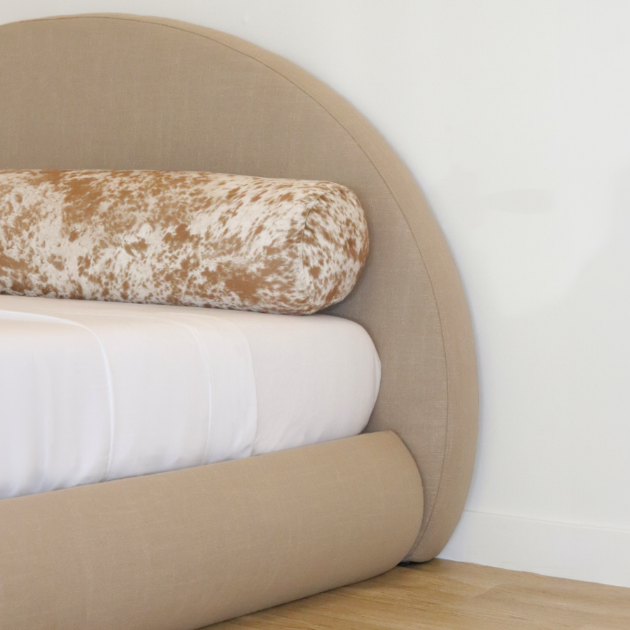 Tan upholstered headboard and bed frame with white bedding and a patterned palomino pillow against a white wall | Luna Set, Sahara | SoftFrame® Designs