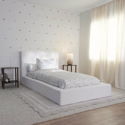 3/4 angle of a white boucle bed set in a childs room with white and green bed sheets decorated with toys and wooden side tables. 