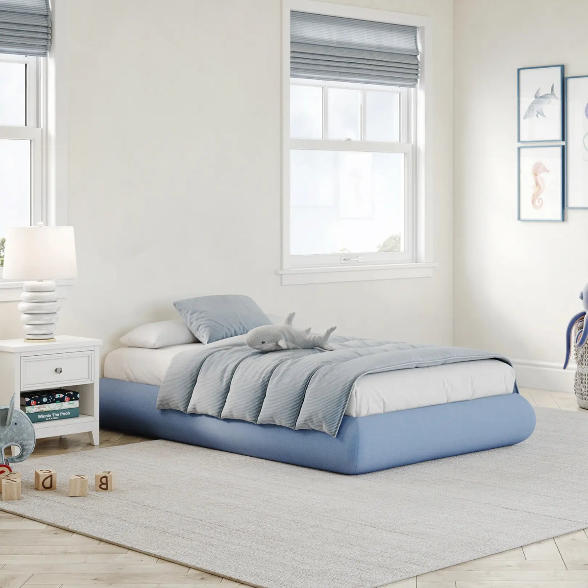A 3/4 view of a kids all cushioned bed frame in sky in a gray kids bed room with big windows with trees. 
