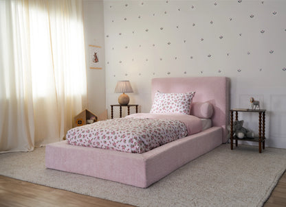 Pink all cushioned bed frame for kids in a twin size with floral sheets and beige curtains.