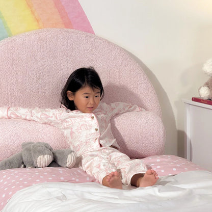 Child in pajamas lying on a pink all cushioned headboard