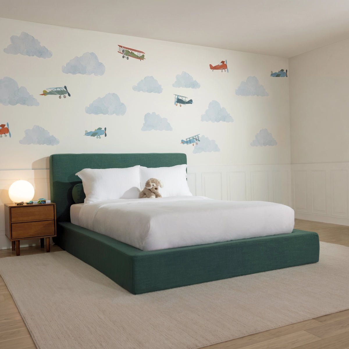 3/4 View of a all cushioned bed frame in the fabric color Forest from softframe designs, decorated with cloud wall decal and toys
