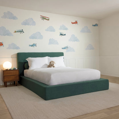 3/4 View of a all cushioned bed frame in the fabric color Forest from softframe designs, decorated with cloud wall decal and toys
