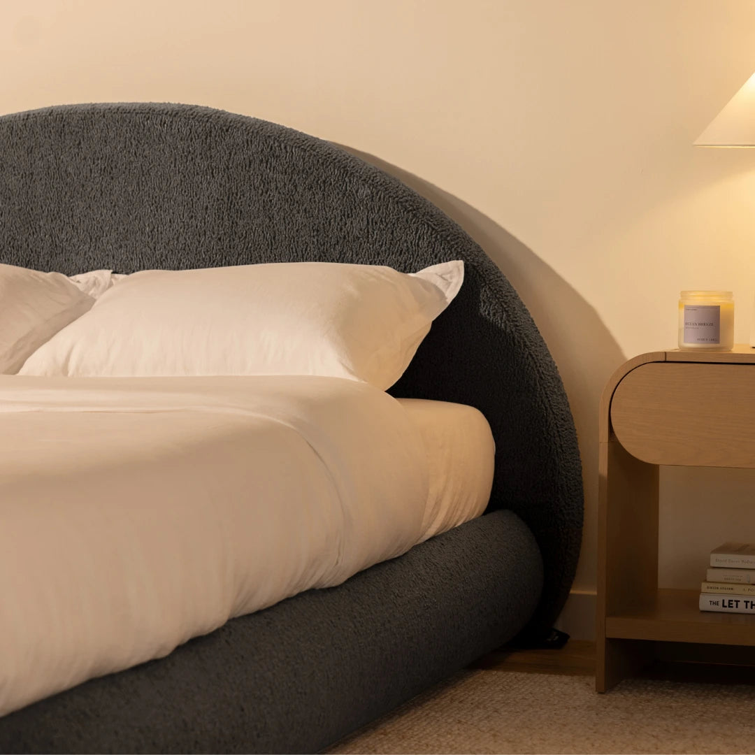 Bedroom with a charcoal grey, soft bed frame and a nightstand featuring books and a small lamp | Luna Set in Storm | SoftFrame® Designs