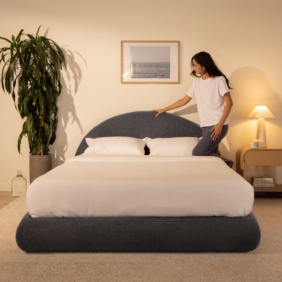 Person pressing on an all-cushioned headboard in a bedroom with a plant and lamp in the background | Luna Set in Storm | SoftFrame® Designs