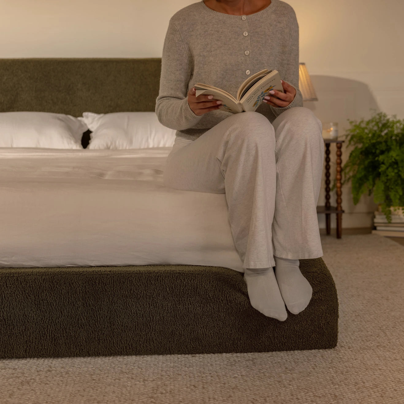 Person sitting on a bed reading a book in a cozy bedroom setting pressing their feet into an all cushioned cloud bed | Ultra Set in Moss | SoftFrame® Designs