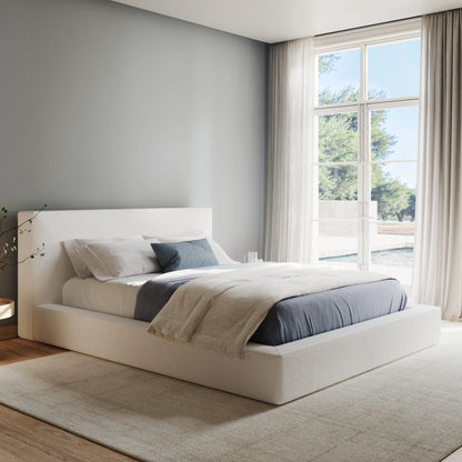 Modern bedroom with a all cushioned bed and neatly made bed in a bright room with large windows.
