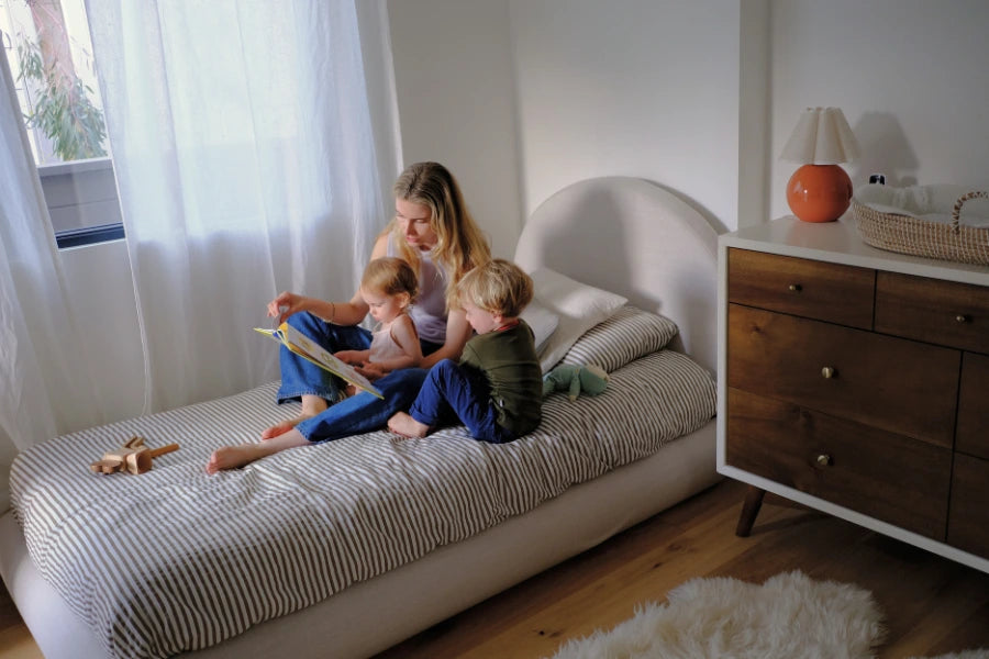 Woman reading to two children on a bed in a bedroom while surrounded by an all cushioned bed frame | SoftFrame Designs