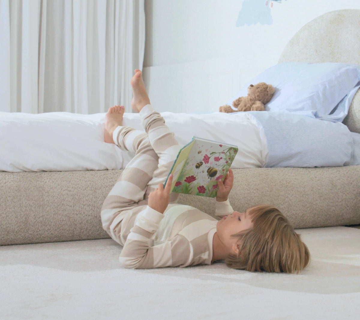 Brown boucle fabric all cushioned bed frame by softframe designs.A child laying on the floor with his feet up rested on the soft all cushioned bed frame