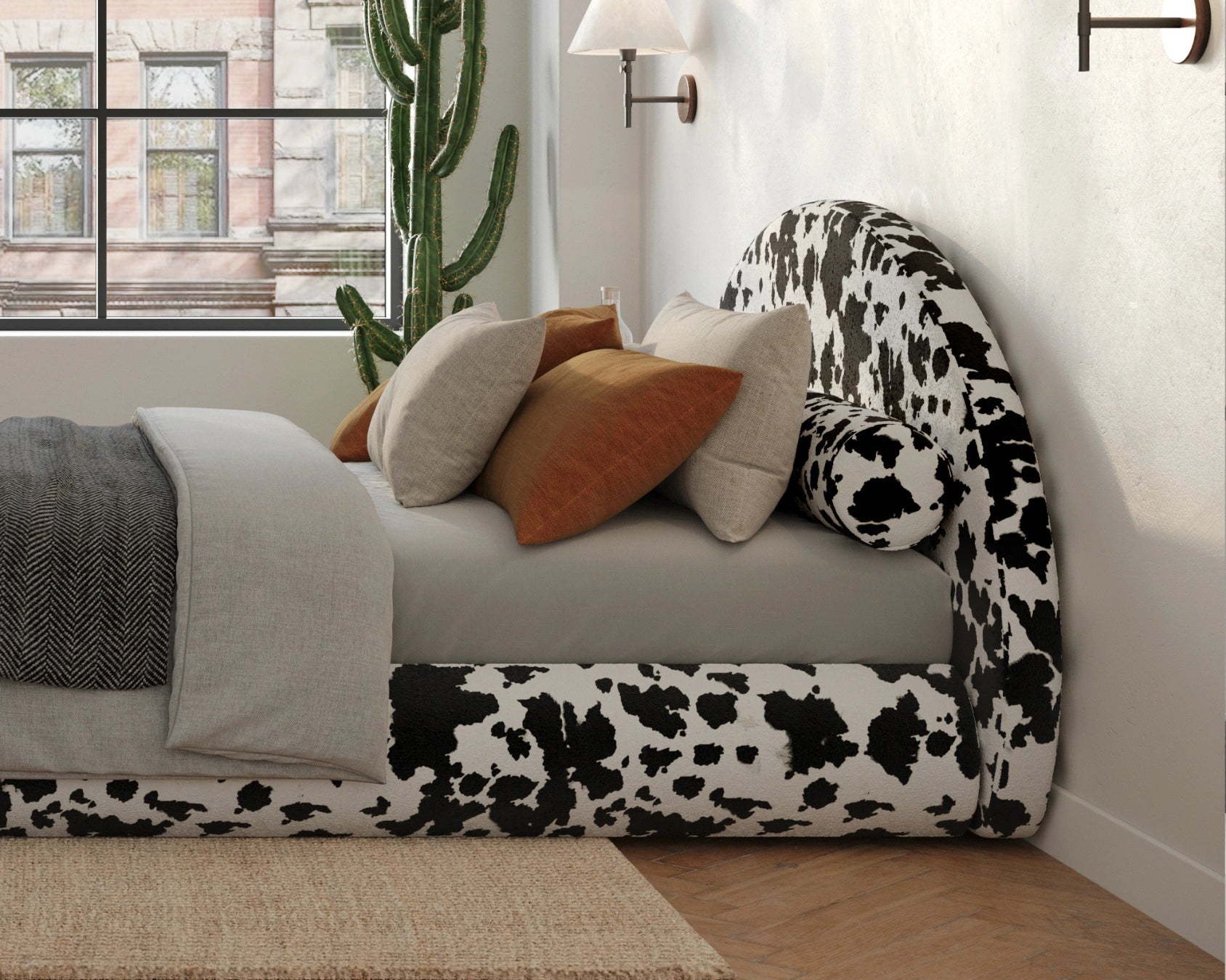 Bed with cow print all cushioned headboard and decorative pillows in a room with a window and plant.
