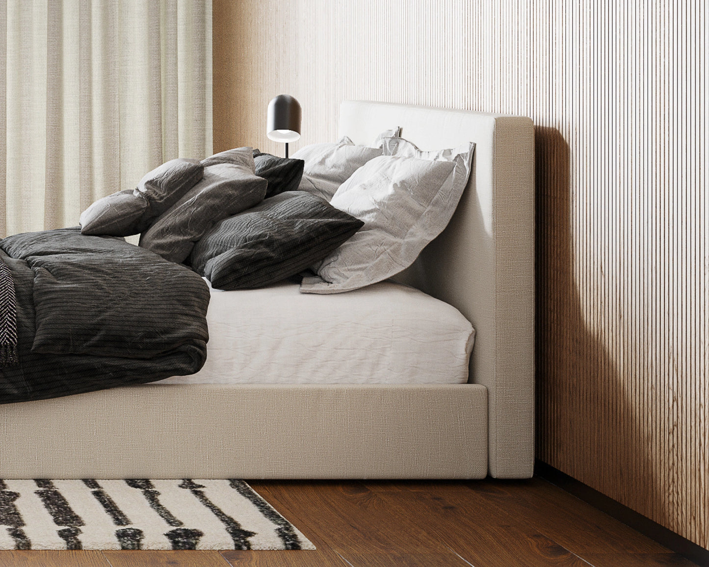 Beige all cushioned  bed with dark gray bedding in a room with wooden flooring and striped rug.