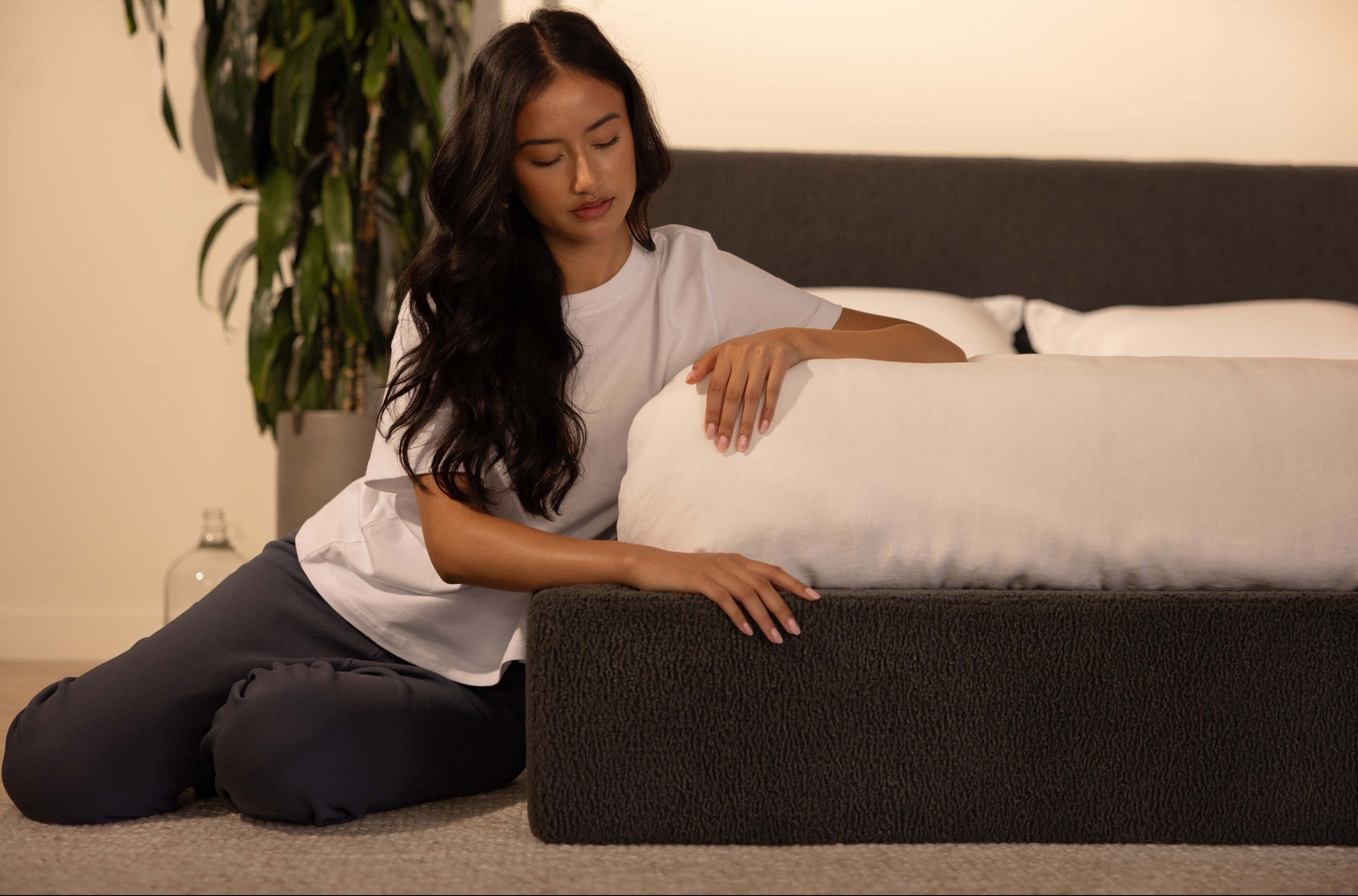 Woman sitting on the floor next to a SoftFrame plush bedframe