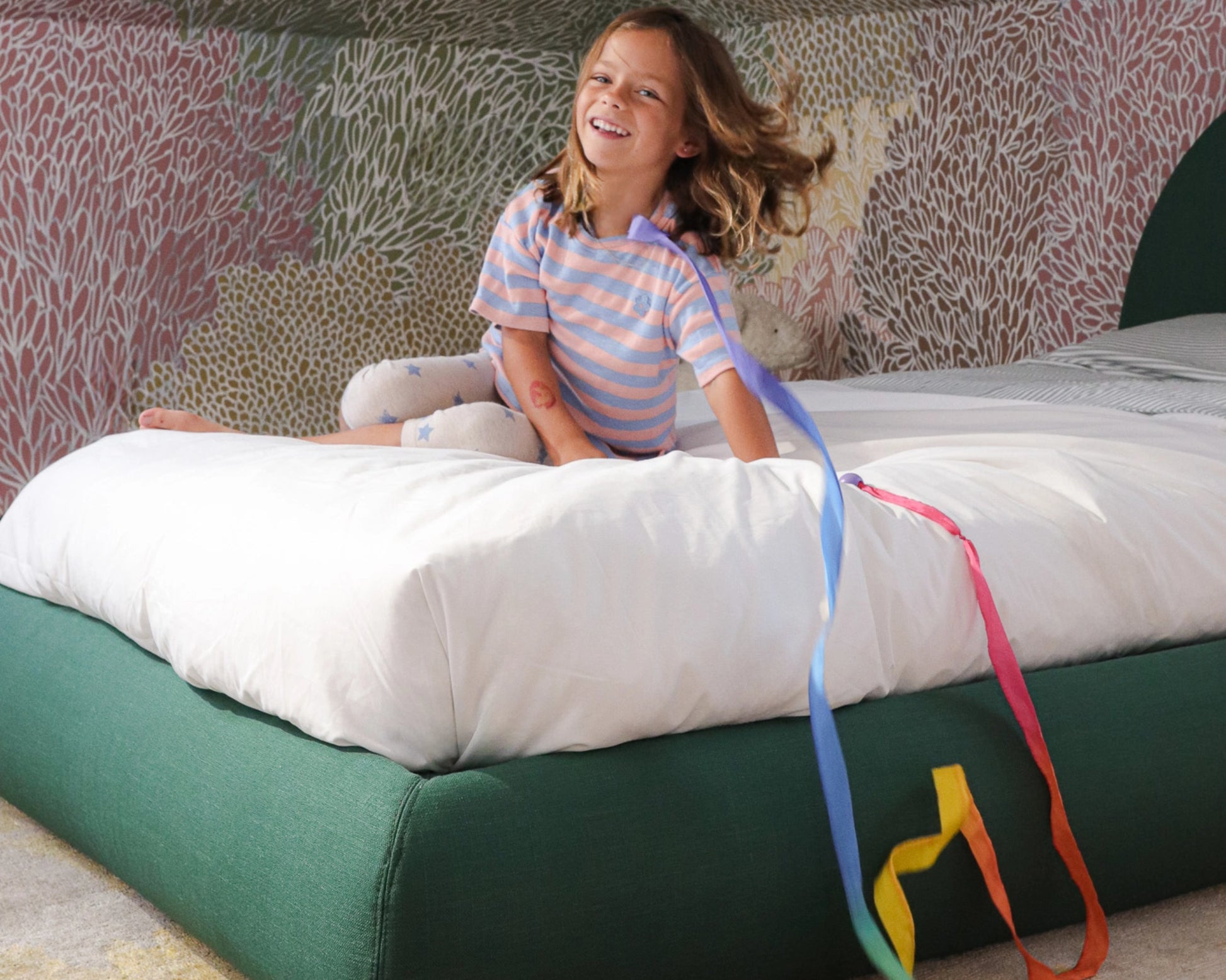 Child sitting on a all cushioned bed frame with colorful ribbons, smiling.