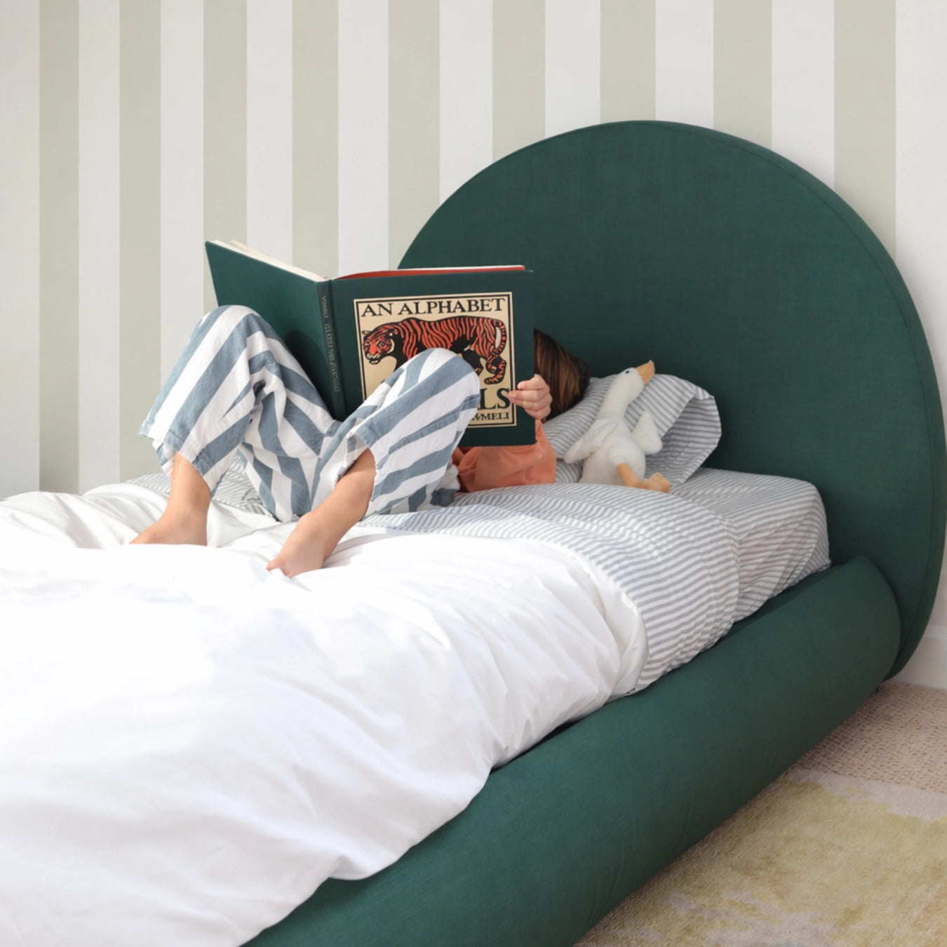 Person reading a book on a green bed with striped wallpaper.