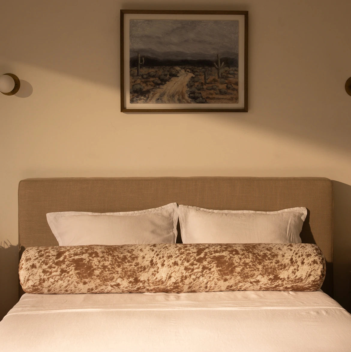 Bedroom with a bed featuring a round pillow, with a painting on the wall | Round Bolster Pillow, Queen, Pony | SoftFrame Designs
