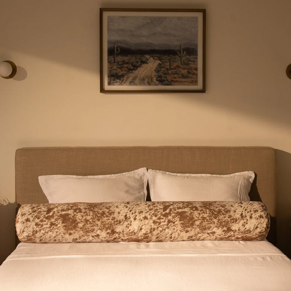 Bedroom with a bed featuring a round pillow, with a painting on the wall | Round Bolster Pillow, Queen, Pony | SoftFrame Designs