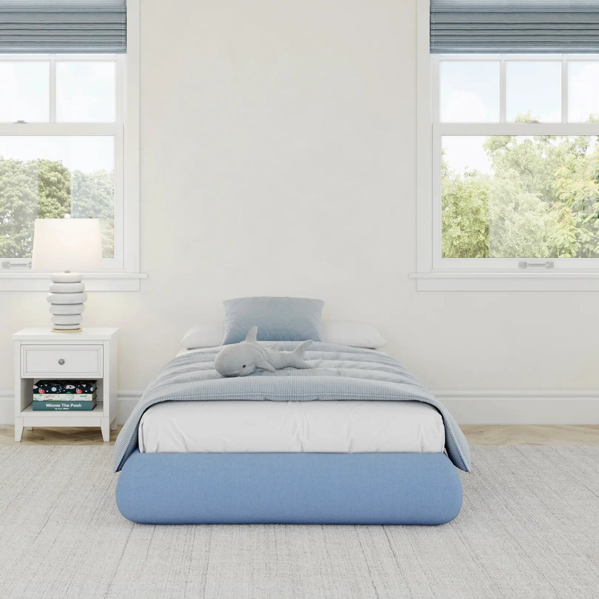 A front view of a kids all cushioned bed frame in sky in a gray kids bed room with big windows with trees. 