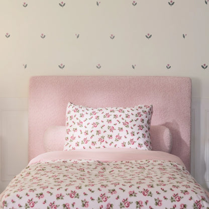 front view of a all cushioned headboard styles with pink floral bedding and a round bolster boucle pillow, with a floral accent wall. 