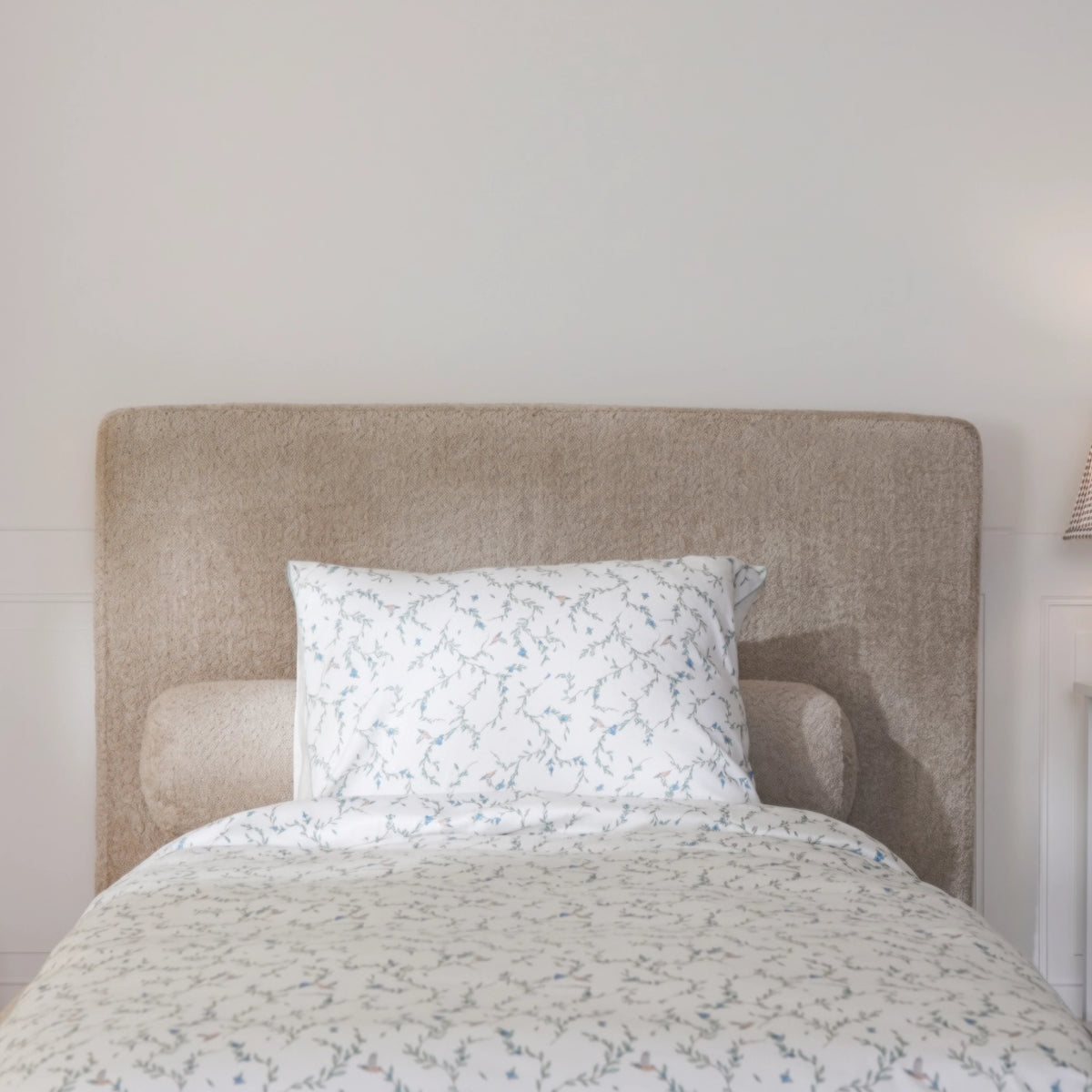 front close up view a a brown all cushioned headboard in the fabric teddy styles with green and white bed sheets
