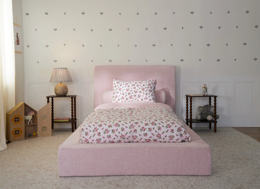 Kids twin all cushioned bed in a pink room with floral sheets and toys on the side. 