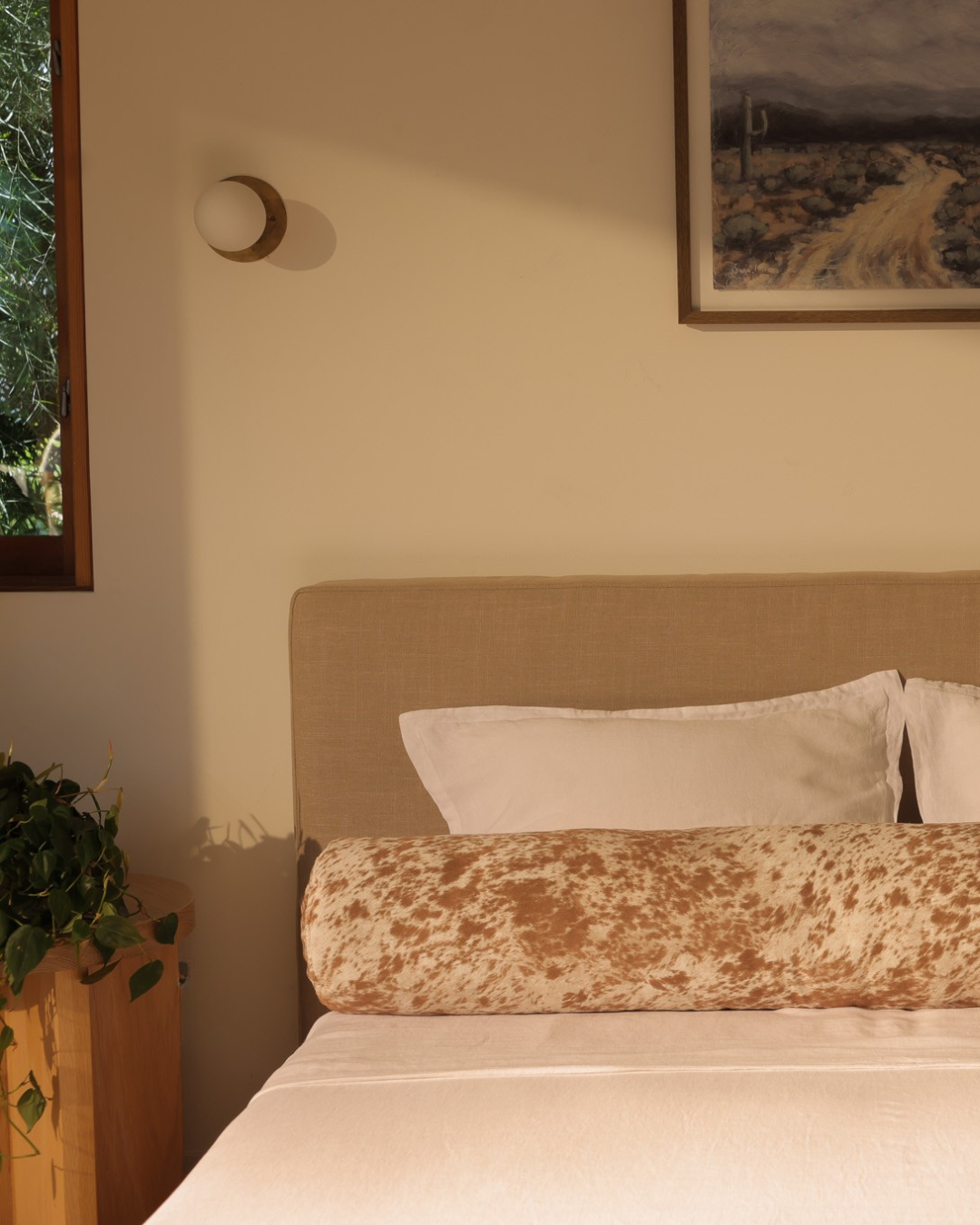 close up of the left side of the round bolster pillow in pony with a desert portrait above the headboard
