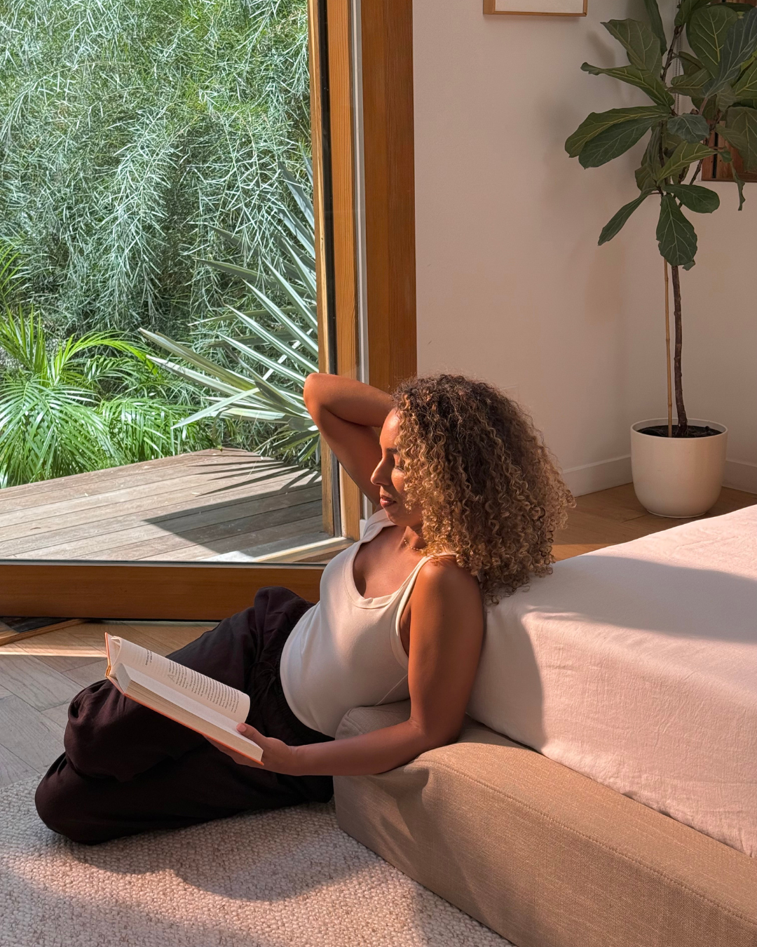 Woman sitting on a bed surrounded by a limited edition, warm beige upholstered bed frame