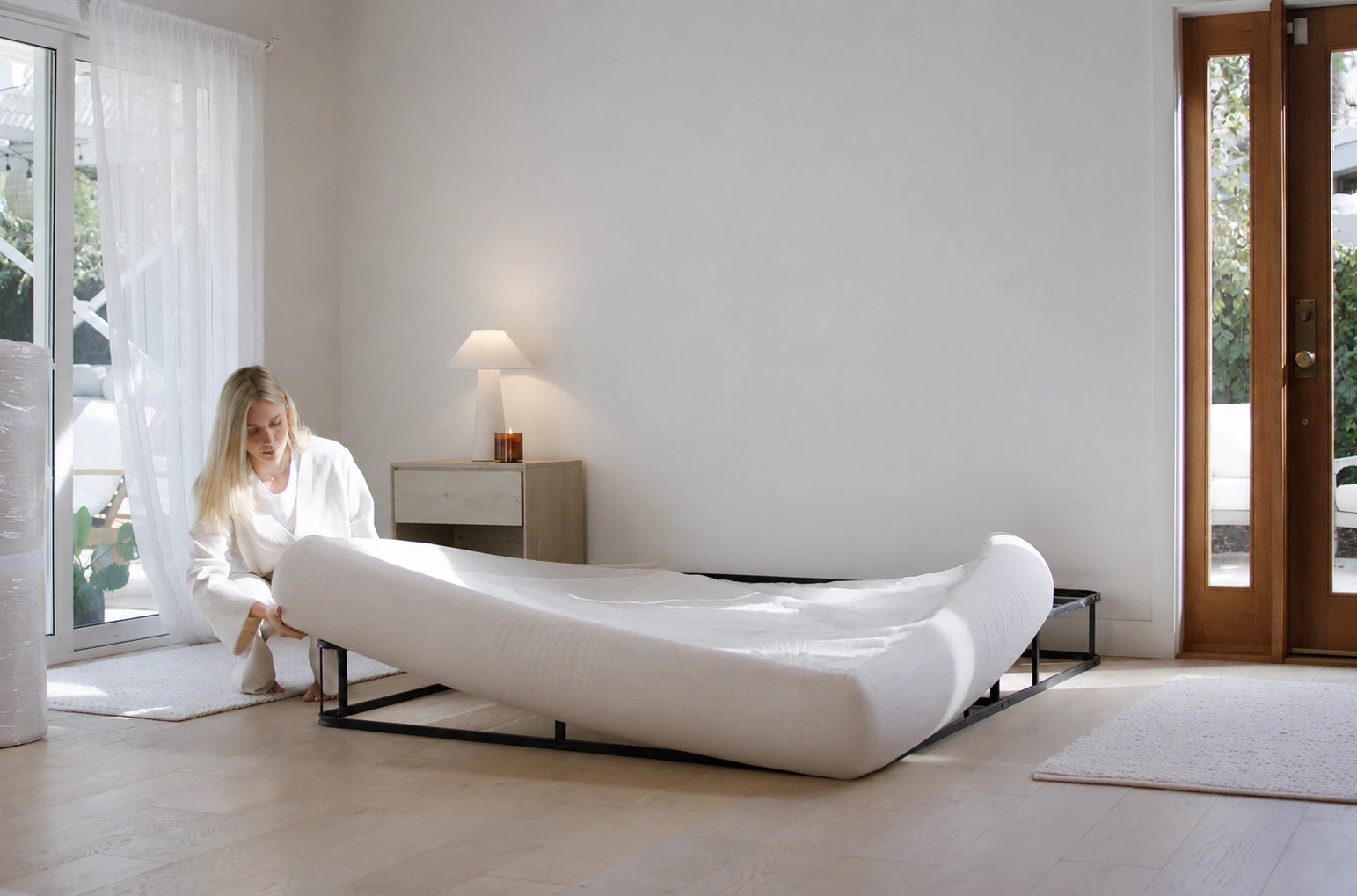 Woman in a bedroom setting up a soft, modern beige bed in a minimalistic room | SoftFrame Designs