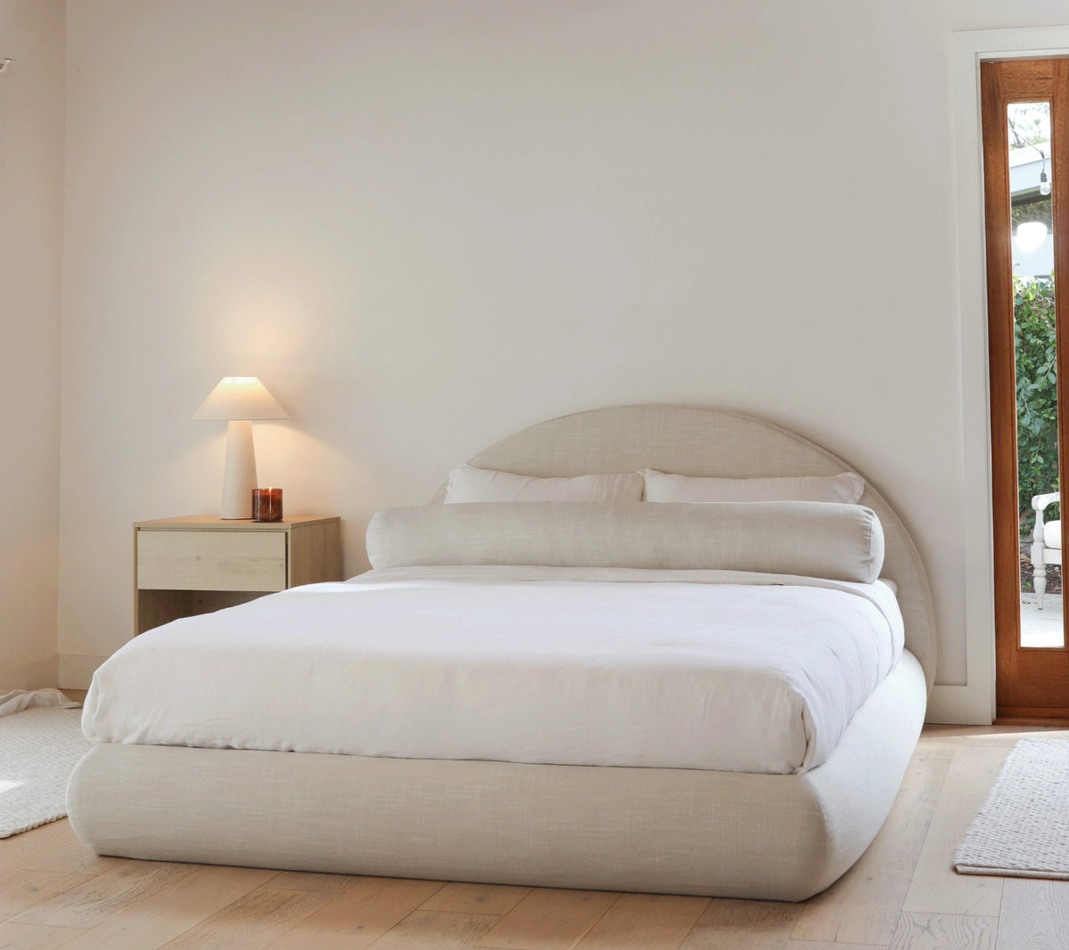 Neatly made curved bed in a minimalistic bedroom with a lamp and nightstand