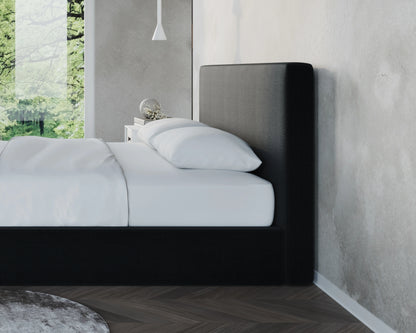 Modern bedroom with a black upholstered all cushioned bed against a gray wall.