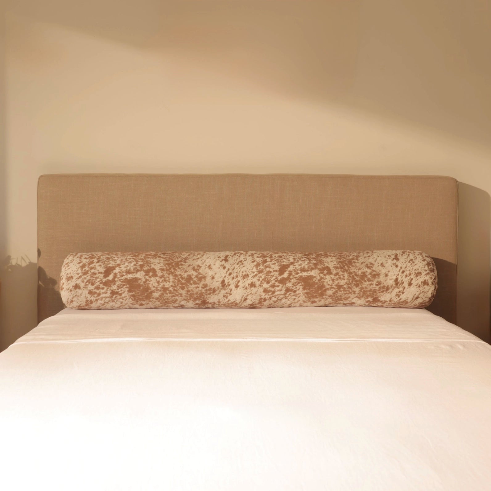 Beige headboard with decorative pillow on a bed against a beige wall