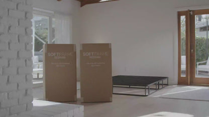 A woman setting up all cushioned ultra bed set from SoftFrame Designs in the Dune color in a airy minimalist room.