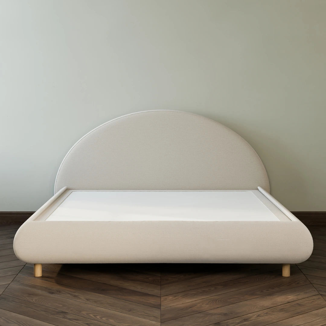 Beige bed with a rounded headboard on a wooden floor against a plain wall