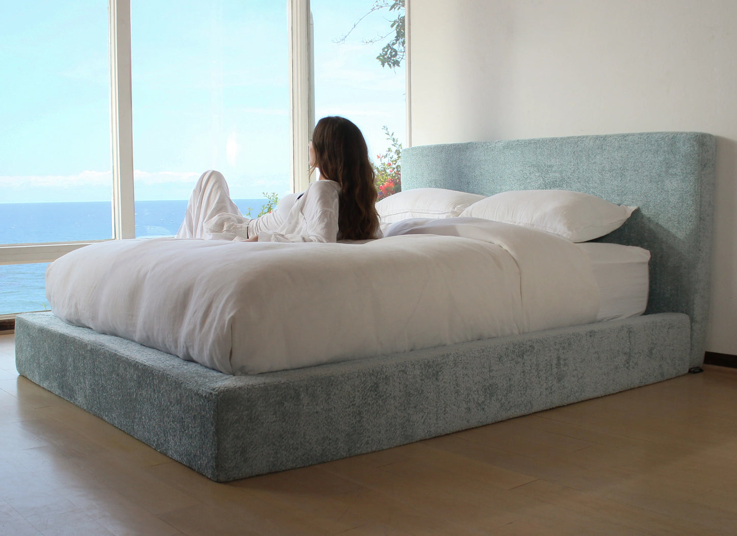 Woman lying on a bed with a large window view of water and sky.