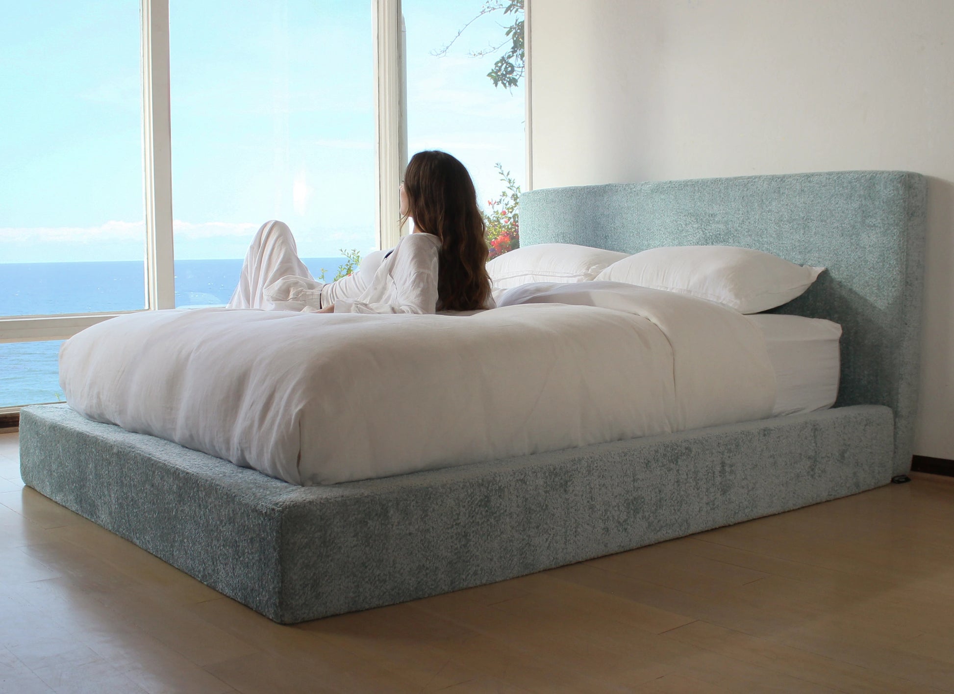Woman lying on a bed with a large window view of water and sky.