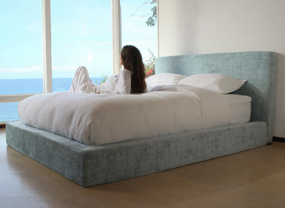 Woman lying on a bed with a large window view of water and sky.
