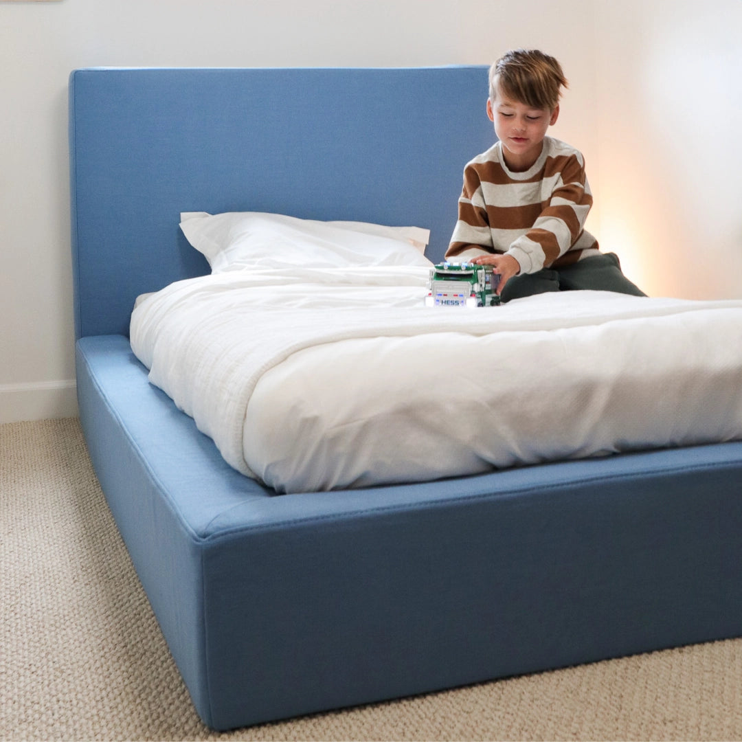 Child sitting on a blue bed with a toy car| White bed sheets| SoftFrame Kids