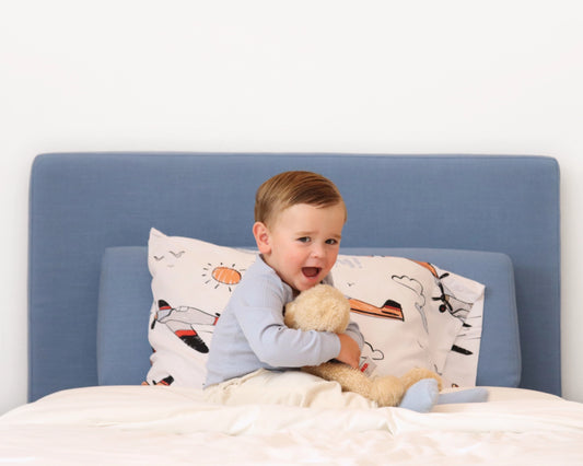Boy on a all cushioned headboard with a teddy bear