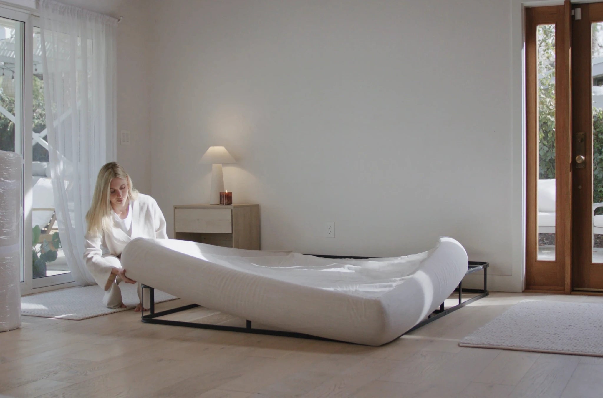 Woman in a bedroom setting up a soft, modern beige bed in a minimalistic room | SoftFrame Designs