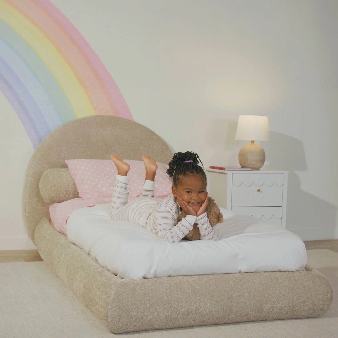 A kids room with a brown all cushioned bed frame and rainbow art 