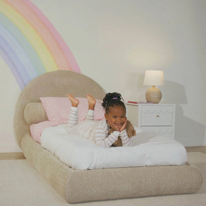 A kids room with a brown all cushioned bed frame and rainbow art 