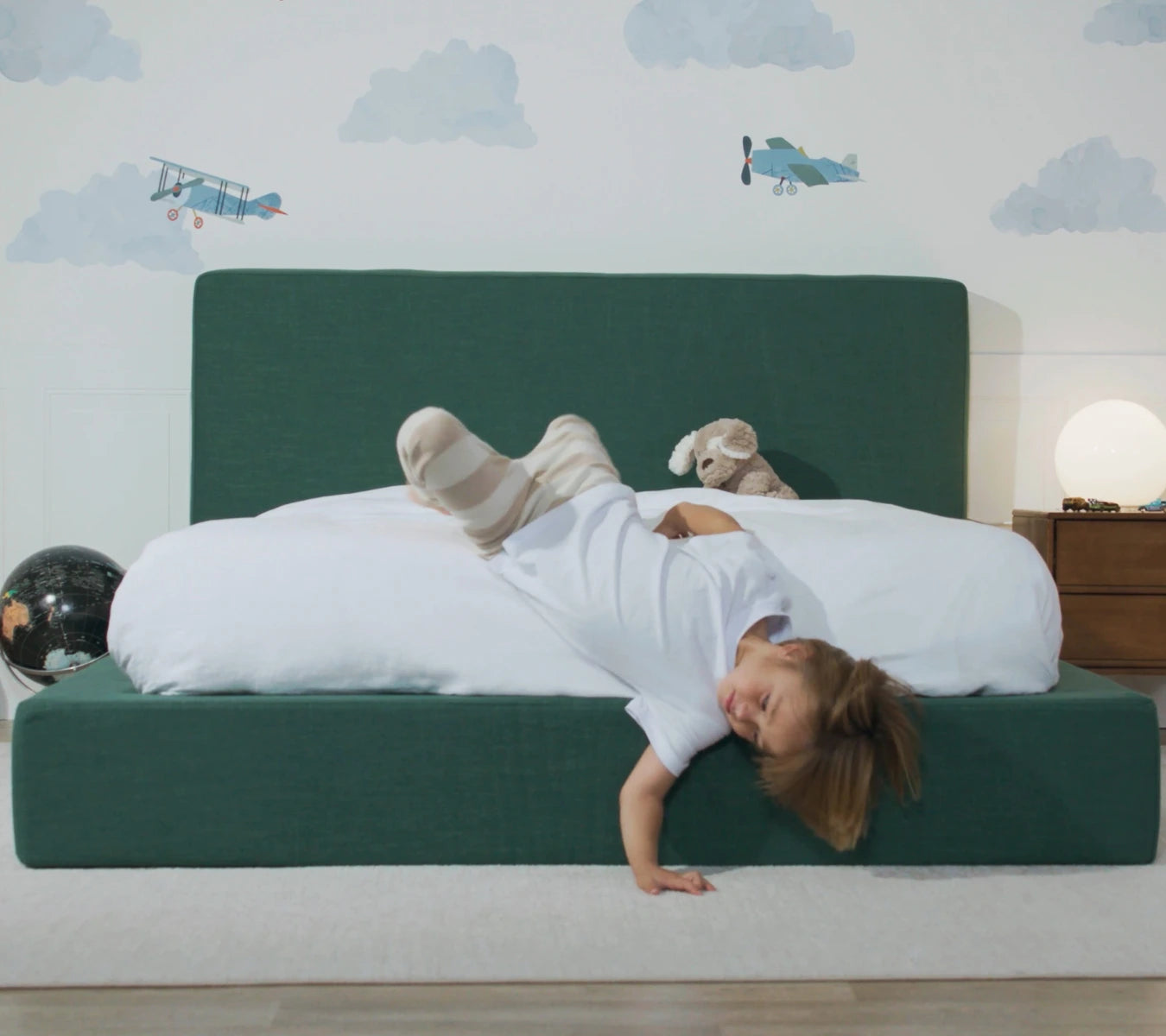Child playing on a green, soft bed frame and headboard set with airplane wall decals | SoftFrame Kids