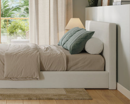 Neatly made bed with beige bedding and green pillows in a bright bedroom.